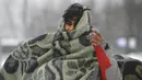 Seorang migran membungkus dirinya dengan selimut saat berjalan melewati salju di kamp Lipa, barat daya Bosnia, Sabtu (26/12/2020). Para imigran membungkus tubuh mereka dalam balutan selimut dan kantong tidur untuk melindungi diri dari serangan angin dingin yang menusuk. (AP Photo/Kemal Softic)