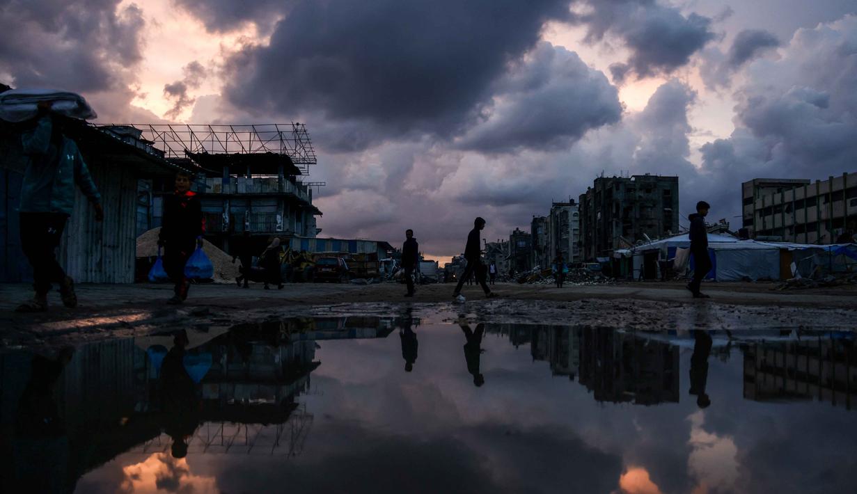 Diperkirakan, sekitar 70 persen lebih bangunan hancur atau rusak parah. Tampak dalam foto, orang-orang berjalan melewati genangan air di lingkungan Al-Saftawi, sebelah barat kota Jabalia di Jalur Gaza utara pada Rabu 10 Desember 2025. (BASHAR TALEB/AFP)
