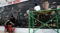 Seniman lokal menyelesaikan mural berjudul 'The Heroes' di Chiang Rai, 18 Juli 2018. Tampak lukisan wajah Saman Gunan, mantan penyelam AL Thailand yang meninggal dunia saat membantu operasi penyelamatan tim sepak bola Wild Boars. (AFP/Lillian SUWANRUMPHA)