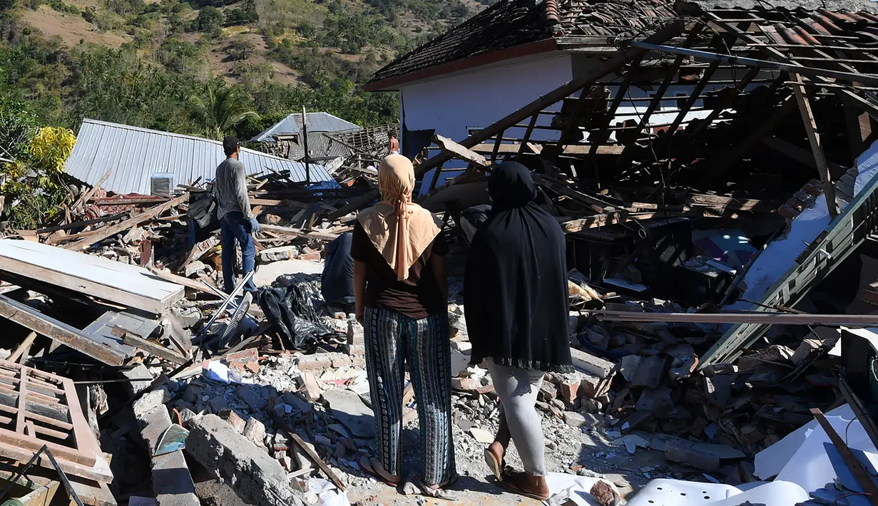 Dua wanita melihat warga menyelamatkan sisa-sisa puing dari rumah yang rusak di Menggala, Lombok Utara, Rabu (8/8). Warga terdampak gempa Lombok mulai mengamankan barang berharga karena kuatir dijarah pihak tidak bertanggung jawab. (AFP/ADEK BERRY)