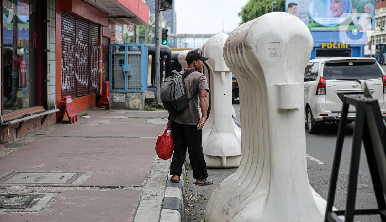 Warga berjalan kaki di samping barrier atau penghalang di kawasan Harmoni, Jakarta, Kamis (27/10/2022). Barrier yang biasa digunakan ketika terjadi demonstrasi Itu menyulitkan pejalan kaki saat melintas di trotoar. (Liputan6.com/Faizal Fanani)