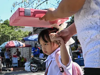 Seorang pria menggunakan tas sekolah untuk melindungi seorang anak dari sengatan matahari saat mereka meninggalkan sekolah di Manila, Filipina pada Senin 3 Maret 2025. (Jam STA ROSA/AFP)