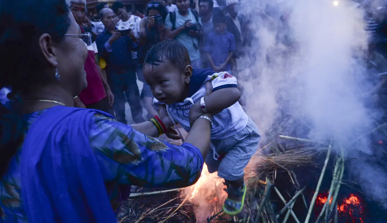 Seorang ibu mengasapi anaknya di sisa pembakaran patung iblis Ghantakarna selama Ghantakarna di kota kuno Bhaktapur, Nepal (30/7/2019). Ritual ini untuk merayakan kekalahan iblis dalam mitos Ghantakarna yang menyimbolkan penghancuran kejahatan. (AFP Photo/Prakash Mathema)