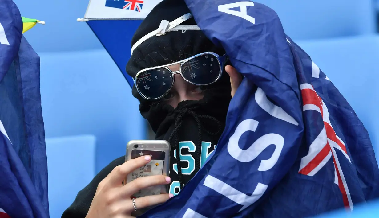 Penonton dengan wajah ditutup menggunakan telepon genggam miliknya saat pertandingan tunggal putra antara petenis Afrika Selatan Kevin Anderson dan petenis Inggris Kyle Edmund di Australia Terbuka di Melbourne (15/1). (AFP Photo/Paul Crock)