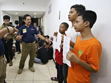 Petugas mengambil gambar sejumlah anak yang tengah memegang surat pernyataan di Polda Metro Jaya, Jakarta, Minggu (18/10). Polisi mengamankan ratusan remaja yang berbuat onar menjelang laga final Piala Presiden di GBK. (Liputan6.com/Immanuel Antonius)