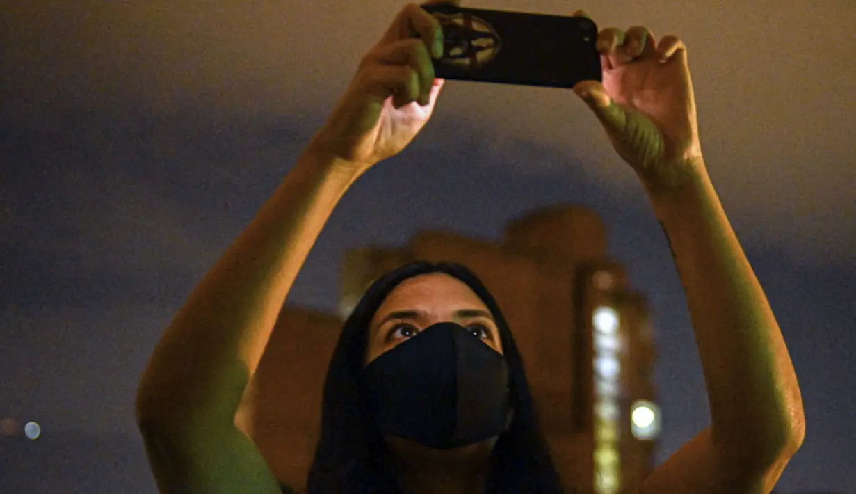 Aktivis Kolombia dan pembuat film Laura Mora, dari @lanuevabandadelaterraza, mengambil foto proyeksi gambar dan slogan di dinding gedung, sebagai bagian dari cara baru untuk melakukan protes di Medellin, Kolombia, pada 9 Agustus 2020. (Pablo PORCIUNCULA/AFP)