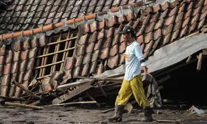 Di beberapa titik, jalan desa tertimbun material vulkanik hingga setinggi atap rumah. Tampak dalam foto, seorang pria menyelamatkan barang-barang dari sebuah rumah yang hancur akibat aliran piroklastik Gunung Semeru di Desa Supiturang, Lumajang, Jawa Timur, pada Jumat 21 November 2025. (Agus Harianto/AFP)