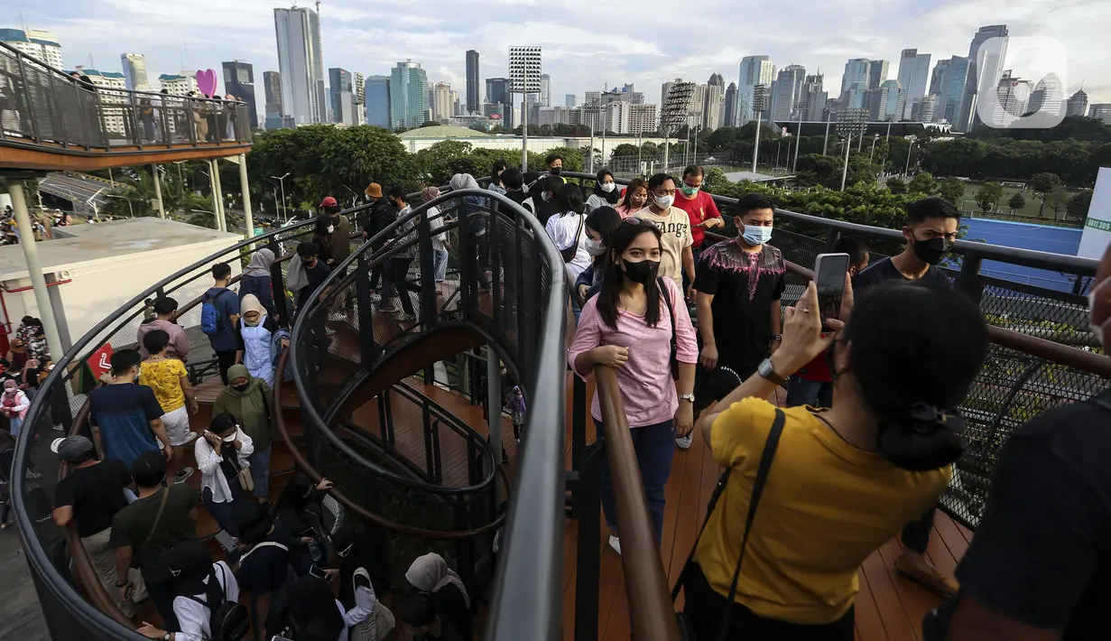 Warga berfoto saat mengisi libur Tahun Baru dengan menikmati pemandangan Kota Jakarta dari Skywalk Senayan Park, Sabtu (1/1/2022). Skywalk Senayan Park kini menjadi salah satu tempat wisata pilihan warga Jakarta lantaran pemandangannya yang instagramable. (Liputan6.com/Johan Tallo)