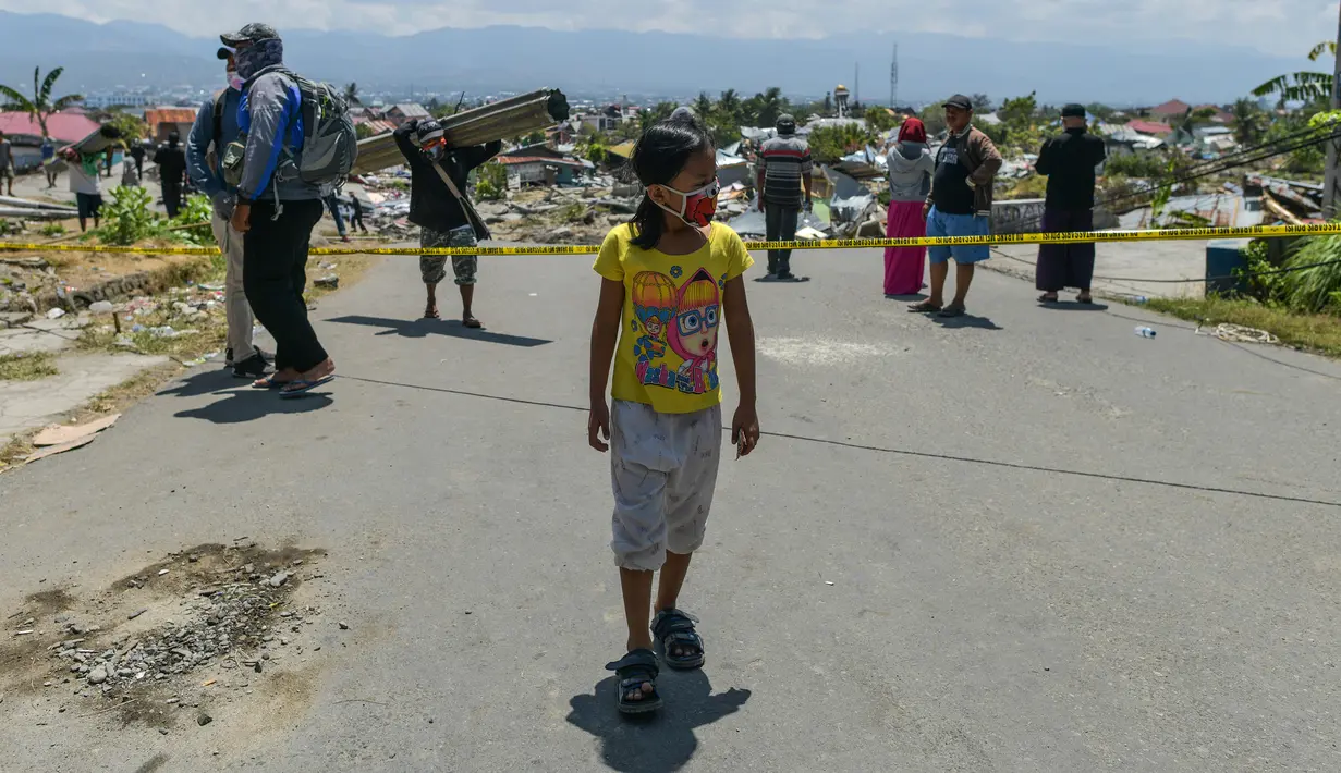 Seorang anak yang mengenakan topeng wajah berjalan melewati puing-puing di desa Perumnas Balaroa, Palu, Selasa (2/10). Data terbaru BNPB menunjukkan, korban tewas akibat tsunami dan gempa di Sulawesi Tengah sudah mencapai 1.347 orang. (AFP/Mohd RASFAN)