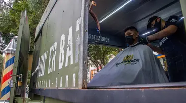 Seorang tukang cukur memotong rambut pelanggan di mobil van atau truck yang diubah menjadi barbershop di sebuah jalan di tengah pandemi virus corona COVID-19, di Mexico City, pada Minggu (6/9/2020). (Photo by CLAUDIO CRUZ / AFP)