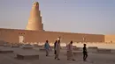 <p>Warga Irak berjalan di usai menaiki menara spiral Malwiya, monumen nasional Irak yang berharga pada pertengahan abad kesembilan, di dalam Kota Arkeologi Samarra, di Samarra, utara Baghdad (26/7/2022). (AFP/Ismael Adnan)</p>