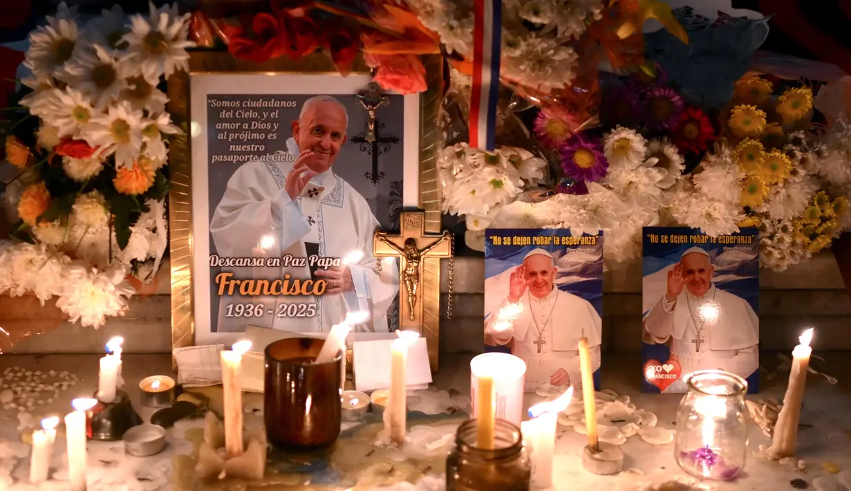 Lilin dan bunga diletakkan di samping foto mendiang Paus Fransiskus di pintu masuk Katedral Buenos Aires, Argentina pada tanggal 21 April 2025. (Luis ROBAYO/AFP)