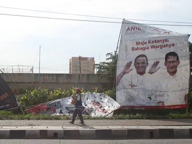 Pejalan kaki melewati alat peraga kampanye Pilkada DKI 2017 yang rusak di kawasan Ancol, Jakarta, Selasa (3/1). Kurangnya pengawasan menyebabkan alat peraga kampanye di sejumlah sudut Ibu Kota mengalami kerusakan. (Liputan6.com/Immanuel Antonius)