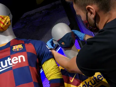 Penjaga toko memasang masker berlogo Barcelona ke Manekin di Toko Asesoris Barcelona, Senin (25/5/2020). Di tengah pandemi virus Corona, Barcelona menjual masker dengan harga 18 euro atau sekitar Rp 291 ribu. (AFP/Lluis Gene)