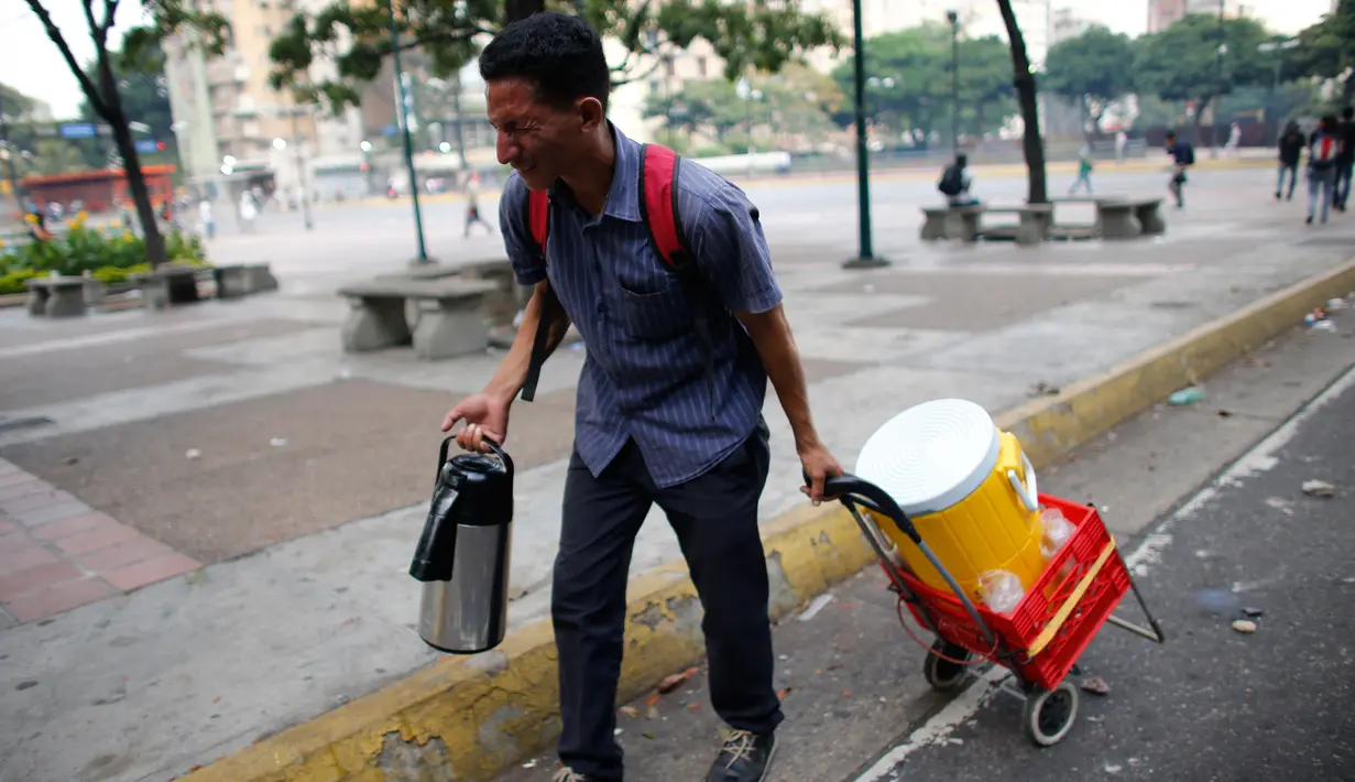 Seorang penjual kopi berjalan saat terjadi bentrokan antara pasukan keamanan dan penentang Presiden Nicolas Maduro di Caracas, Venezuela, (26/3). (AP Photo / Ariana Cubillos)