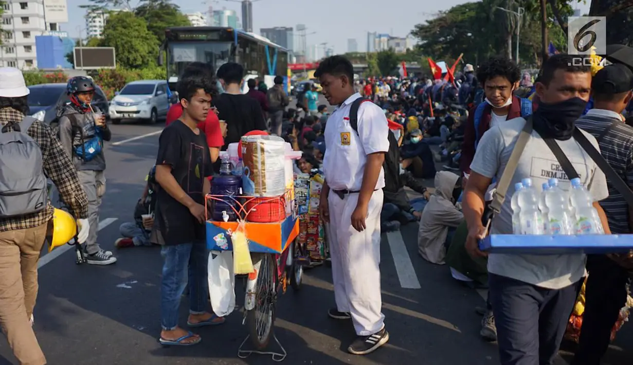 Pedagang melayani pembeli minuman saat berjualan di antara massa aksi di jalan tol dalam kota yang berada di depan Gedung DPR RI, Jakarta, Senin (30/9/2019). Adanya aksi unjuk rasa di sekitar lokasi dimanfaatkan para pedagang asongan untuk mencari rezeki. (Liputan6.com/Immanuel Antonius)