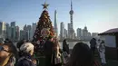 Orang-orang mengambil gambar pohon Natal yang dihias di sepanjang Shanghai Bund menghadap Distrik Keuangan Pudong di Shanghai pada 17 Desember 2023. (AP Photo/Wayne Zhang)
