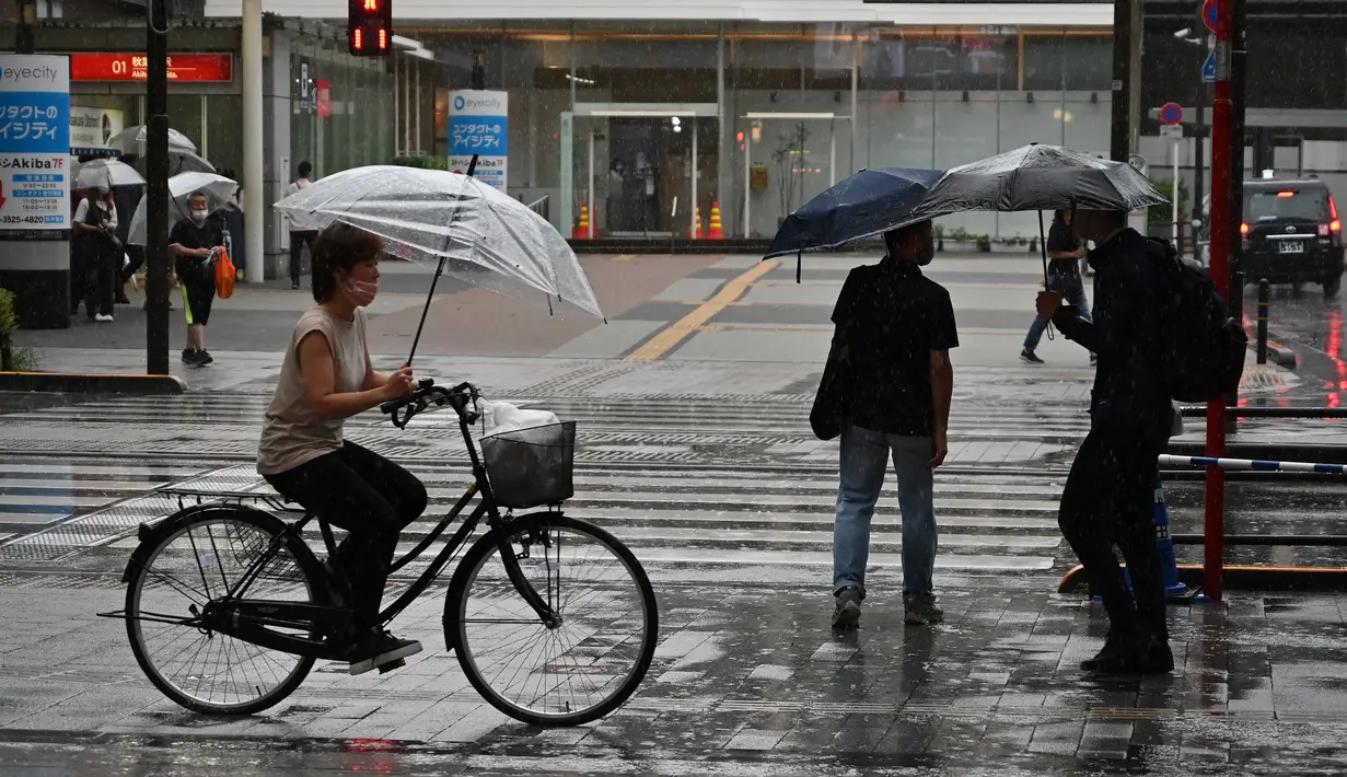 Seorang wanita mengendarai sepeda saat hujan lebat di distrik Akihabara Tokyo (13/8/2022). Hujan lebat yang dibawa oleh Badai Tropis Meari melanda daerah tersebut. (AFP/ Richard A. Brooks)