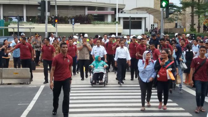 Presiden Jokowi dan Gubernur DKI Anies Baswedan yang memegang kursi roda ibundanya, Aliyah Rasyid menyeberang jalan menggunakan pelican crossing di Jalan Sudirman, Jakarta Pusat, Kamis (2/8/2018). (Liputan6.com/Hanz Jimenez Salim)