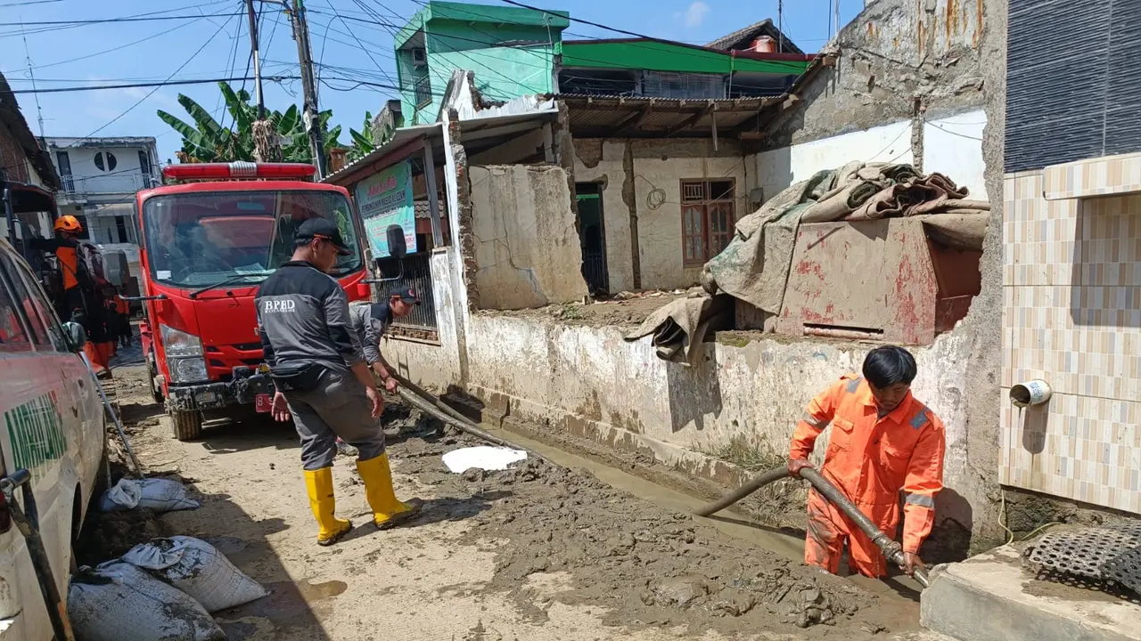 Personel BPBD Kota Bekasi membersihkan sisa-sisa lumpur akibat banjir yang masih terdapat di jalan-jalan umum, menggunakan mobil pemadam kebakaran.