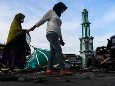 Dua wanita yang terkena dampak gempa berjalan melewati Masjid Raya Baiturrahman yang runtuh di Palu, Sulawesi Tengah, Rabu (3/10). Meski kubah dan beberapa dinding masjid runtuh, namun menaranya masih kokoh berdiri. (AFP PHOTO / JEWEL SAMAD)