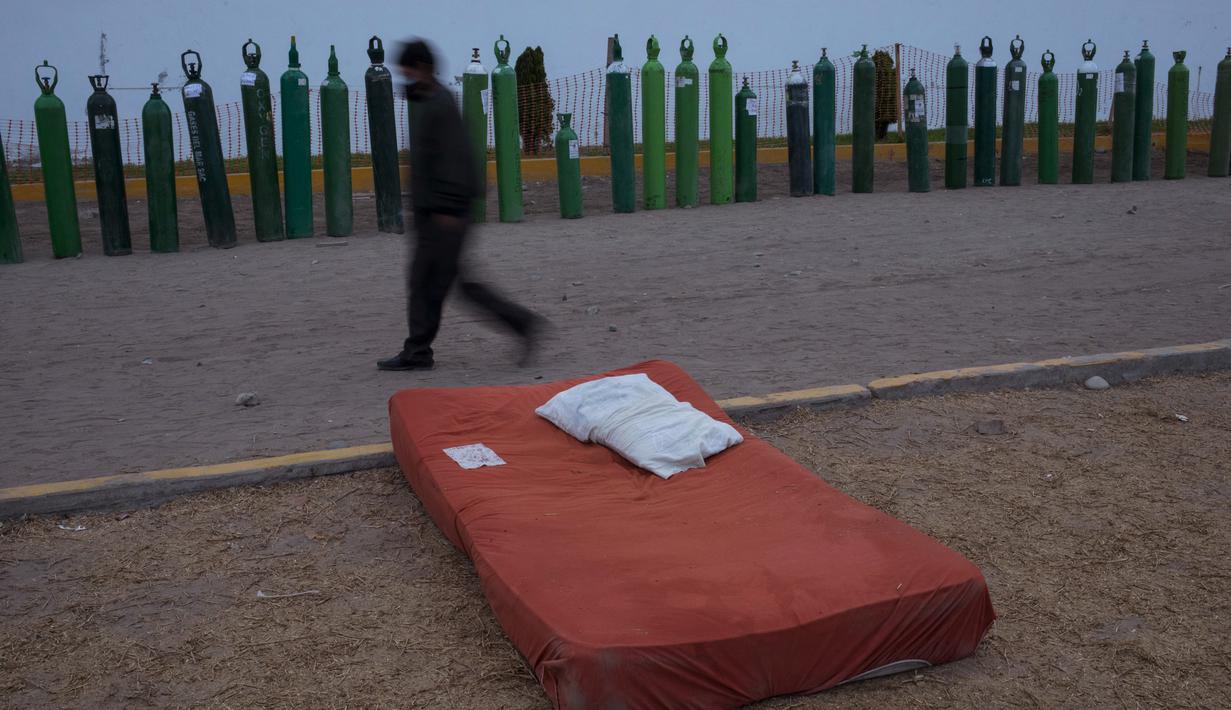 Seorang pria berjalan melewati barisan tabung oksigen kosong di luar toko tempat orang menunggu untuk mengisi tabung mereka di Villa El Salvador, Lima, Peru, Selasa (6/4/2021). Warga Peru terus berjuang mendapatkan oksigen medis untuk merawat pasien COVID-19. (AP Photo/Rodrigo Abd)