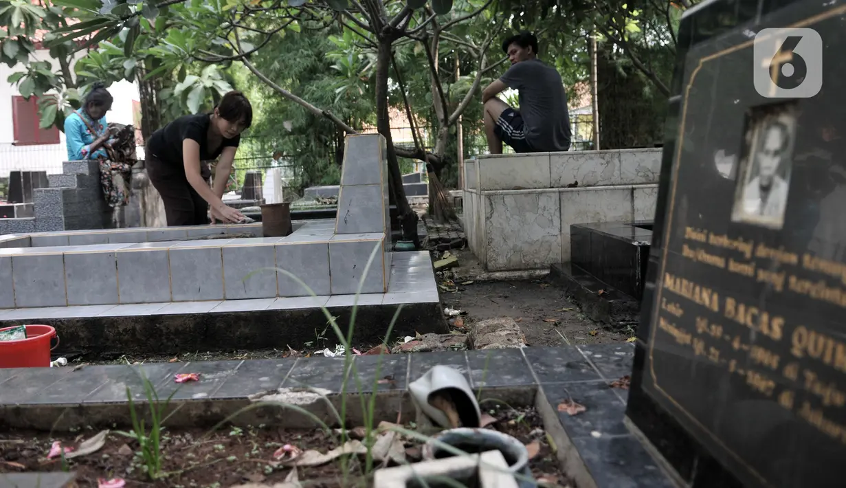 Keluarga membersihkan makam saat ziarah di kompleks pemakaman Gereja Tugu, Semper, Jakarta, Senin (23/12/2019). Warga keturunan Portugis melakukan ziarah ke makam keluarga mereka untuk merawat makam sekaligus mendoakan keluarga yang telah meninggal dunia. (merdeka.com/Iqbal Nugroho)