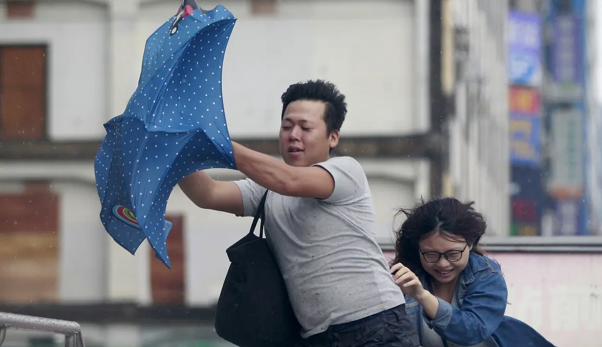 Dua orang memegang payung sambil berjalan menghindari angin kencang yang disebabkan topan Dujuan di Taipei, Taiwan, Senin (28/9). Ribuan orang diungsikan untuk menghadapi topan raksasa Dujuan yang diprediksikan akan menyerang Taiwan.(REUTERS/Pichi Chuang)