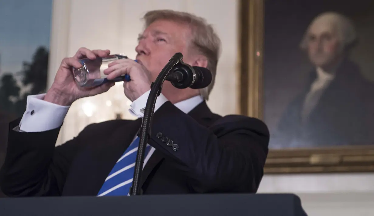 Presiden AS, Donald Trump meminum botol air mineral disela menyampaikan pidato di Ruang Diplomatik Gedung Putih, Rabu (15/11). Sementara itu warganet justru mengkritik Trump yang meminum air mineral impor merek Fiji Water. (MARK WILSON/GETTY IMAGES/AFP)