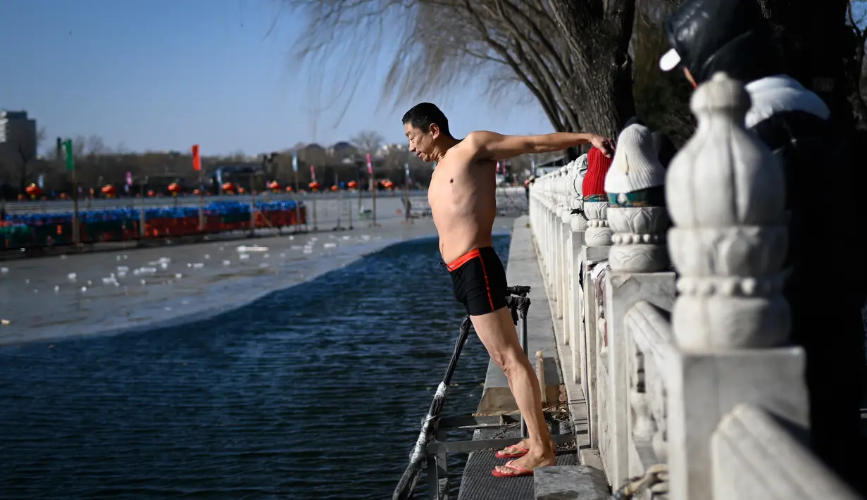 Seorang pria bersiap untuk berenang di sebuah danau yang airnya sebagian membeku di Beijing pada Senin (30/12/2019). Penduduk lokal banyak menggemari kebiasaan berenang di musim dingin dimana banyak sungai dan danau-danau mulai membeku. (WANG ZHAO / AFP)