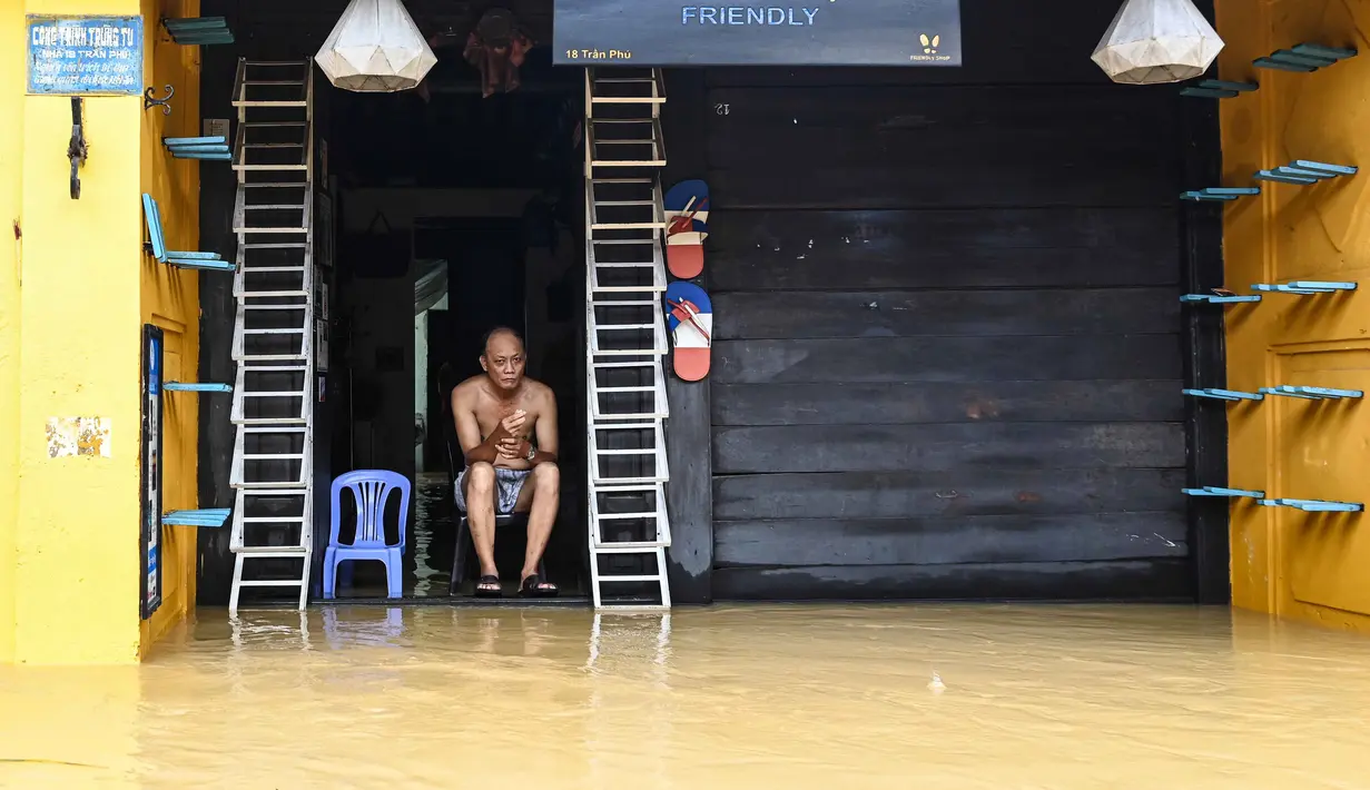 Seorang pria duduk di pintu masuk toko yang terendam banjir setelah hujan deras di Hoi An, Vietnam, Kamis 30 Oktober 2025. Badan Penanggulangan Bencana Nasional Vietnam menyebut bahwa curah hujan ekstrem telah melampaui rekor tertinggi yang pernah tercatat dalam satu hari penuh di wilayah tersebut. (NHAC NGUYEN/AFP)
