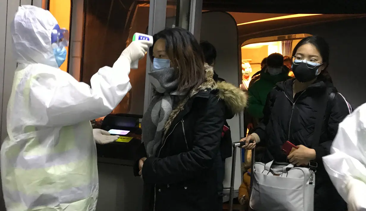 Petugas kesehatan berjas Hazmat memeriksa suhu tubuh penumpang yang datang dari kota Wuhan di bandara Beijing (22/1/2020). Virus corona jenis baru ini ditemukan pertama kali di Wuhan, Provinsi Hubei, Tiongkok. Virus ini diyakini berasal dari pasar makanan laut segar di Wuhan. (AP Photo/Emily Wang)