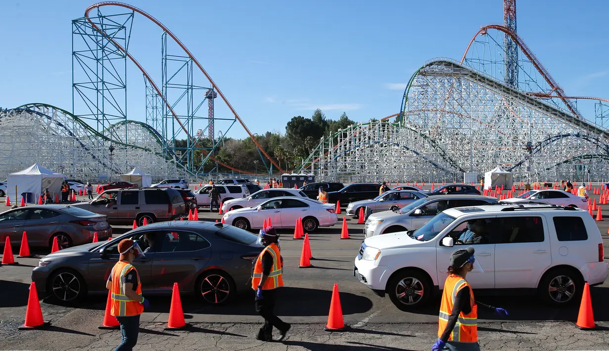 Relawan berjalan saat orang-orang yang telah menerima vaksin berada di dalam kendaraan mereka di pusat vaksinasi COVID-19 drive-thru massal di tempat parkir Six Flags Magic Mountain di Valencia, California, Selasa (2/2/2021). Mario Tama/Getty Images/AFP)