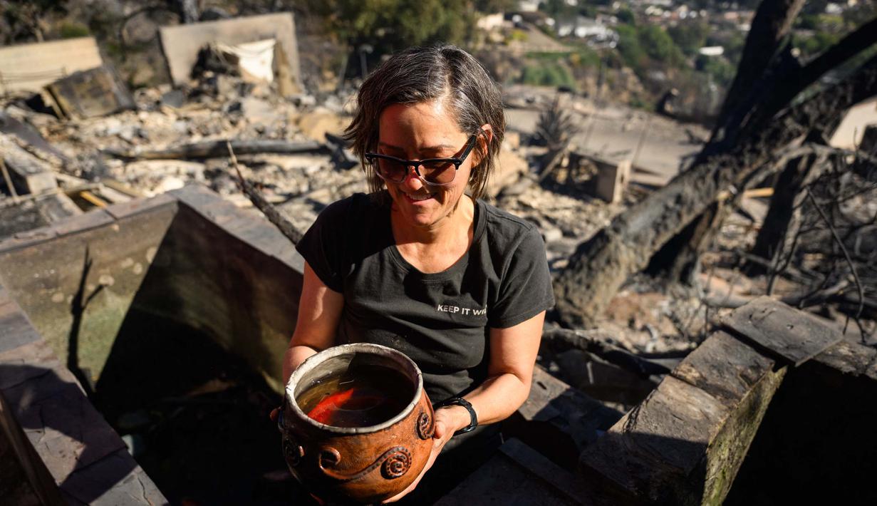 Setelah kobaran api berhasil dikendalikan, pemilik rumah berusaha menyelamatkan barang dan benda yang tersisa. Tampak dalam foto, Robin Wallace menunjukkan ikan peliharaannya di rumah keluarganya di West Highland Drive yang hancur akibat kebakaran hutan dan gunung pada 8 November 2024 di Camarillo, California. (Patrick T. Fallon/AFP)