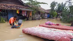 Seorang warga mengeringkan kasur dan barang-barang rumah tangga lainnya dari rumahnya yang terendam banjir di desa Sukajaya di Serang (1/3/2022).  Banjir merendam Kota Serang akibat hujan deras yang turun sejak Senin malam (28/2/2022) hingga hari ini. (AFP/Dziki Oktomauliyadi)