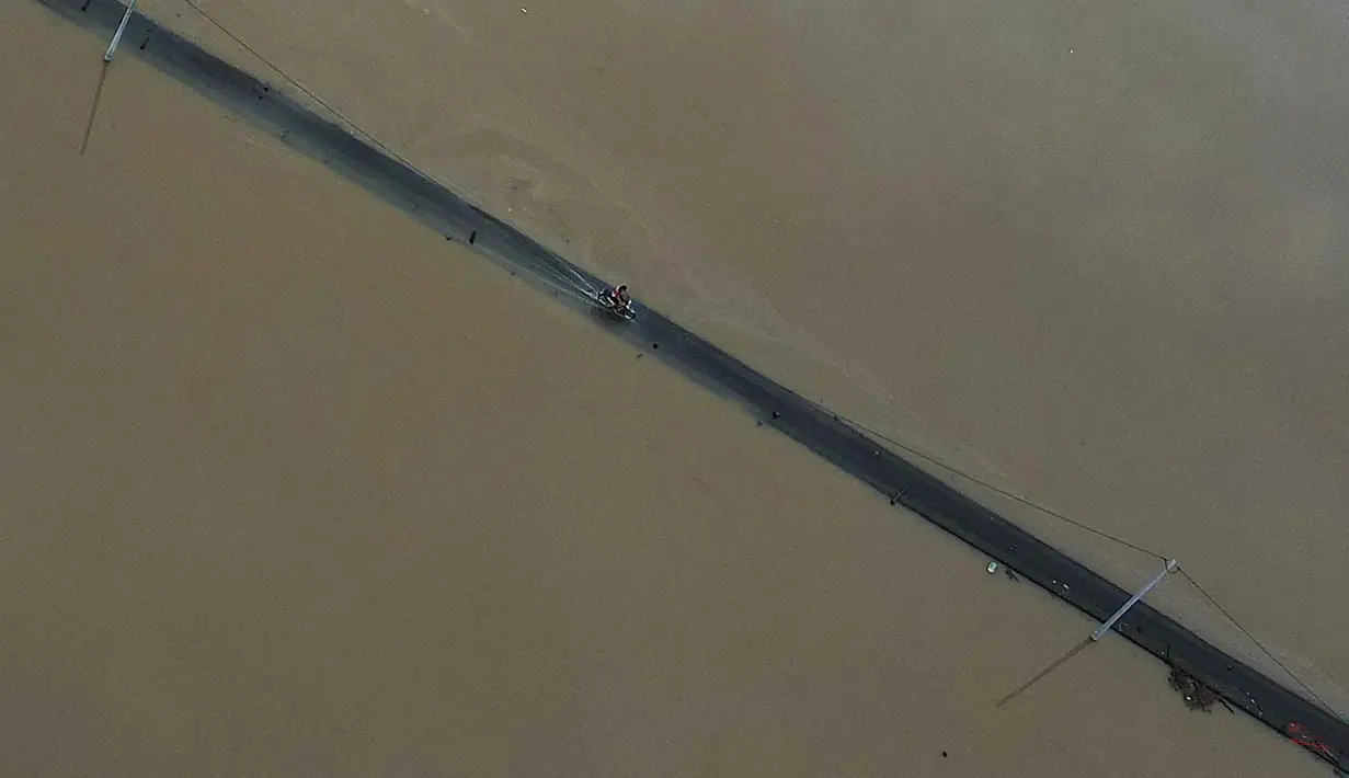 Dalam hitungan jam, air yang semula hanya menggenangi jalan berubah menjadi arus deras yang masuk ke rumah-rumah warga. Tampak foto udara memperlihatkan seorang pengendara yang sedang berkendara di jalan yang terendam banjir di Kangar, negara bagian Perlis, Malaysia utara, pada Jumat 28 November 2025. (Mohd RASFAN/AFP)