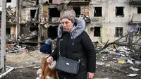 Seorang wanita berjalan di depan bangunan yang rusak setelah peluru militer Rusia menghantam di Koshytsa Street, Kiev, Ukraina (25/2/2022). Ledakan di Kiev memicu kekerasan setelah Presiden Rusia Vladimir Putin menentang peringatan Barat untuk melancarkan invasi darat skala penuh. (AFP/Daniel Leal)