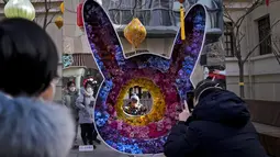 Wanita melihat balita berpose untuk fotodengan dekorasi bunga berbentuk kelinci di shopping street pejalan kaki Qianmen pada hari pertama liburan Tahun Baru Imlek di Beijing, Minggu (22/1/2023). Orang-orang di seluruh China merayakan Tahun Baru Imlek pada hari Minggu dengan pertemuan keluarga besar dan kerumunan orang mengunjungi kuil-kuil setelah pemerintah mencabut kebijakan "nol-COVID" yang ketat, menandai perayaan meriah terbesar sejak pandemi dimulai tiga tahun lalu. (AP Photo/Andy Wong)