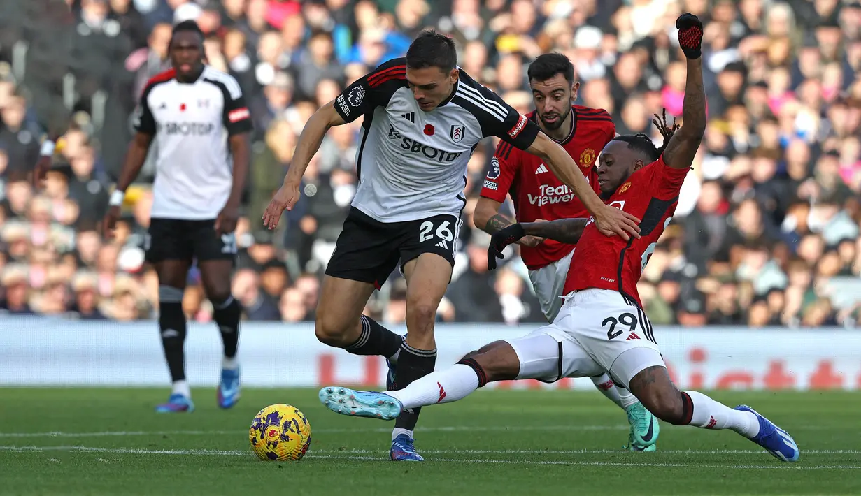Pemain MU, Aaron Wan-Bissaka (kanan), berusaha menghalau bola dari pemain Fulham, Palinha (tengah) dalam pekan ke-11 Premier League 2023/2024 yang berlangsung di Stadion Craven Cottage, London, Sabtu (4/11/2023) malam WIB. (AFP/Adrian Dennis)
