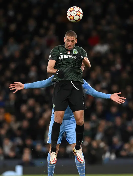 Striker Sporting Lisbon Islam Slimani mengalahkan bek Manchester City Aymeric Laporte untuk menyundul bola pada leg kedua babak 16 besar Liga Champions, Kamis (10/3/2022) dini hari WIB. Manchester City tetap melaju ke perempat final meski bermain imbang 0-0 dengan Sporting Lisbon. (Paul ELLIS/AFP)