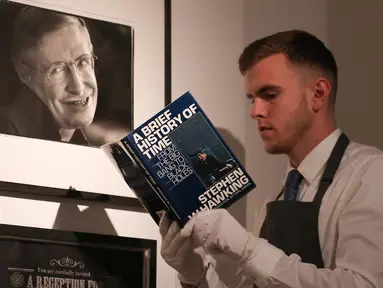 Asisten galeri berpose dengan salinan buku “A History of Time” yang ditandatangani dengan cap jempol oleh fisikawan Stephen Hawking selama sesi pemotretan untuk acara pelelangan di Balai Lelang Christie, London, Selasa (30/10). (Daniel LEAL-OLIVAS/AFP)