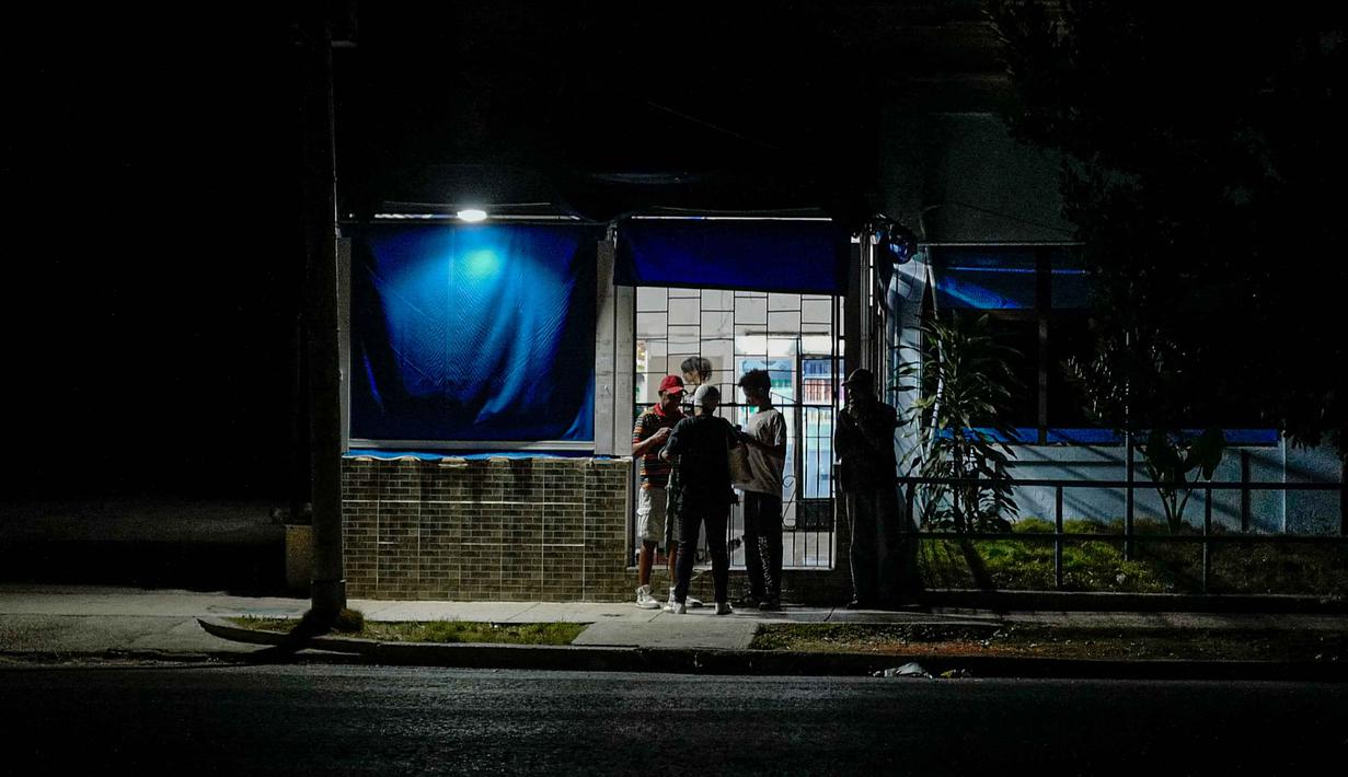 Saat malam tiba, warga di ibu kota Havana terpaksa menggunakan energi alternatif sebagai penerangan. Tampak dalam foto, orang-orang berkumpul di dekat sebuah bisnis swasta dengan generator listrik selama pemadaman listrik nasional di Havana, Kuba pada 21 Maret 2026. (ADALBERTO ROQUE/AFP)