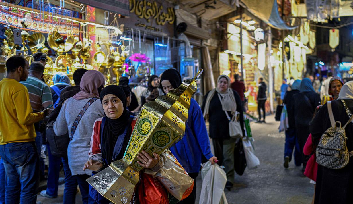 Untuk diketahui, lentera fanous merupakan lampion tradisional khas Mesir yang digunakan untuk menyambut bulan suci Ramadan. Tampak dalam foto, seorang wanita Mesir membawa lentera tradisional, yang dikenal secara lokal sebagai 'Fanous Ramadan', di pusat Kairo pada Kamis 12 Februari 2026. (Khaled DESOUKI/AFP)