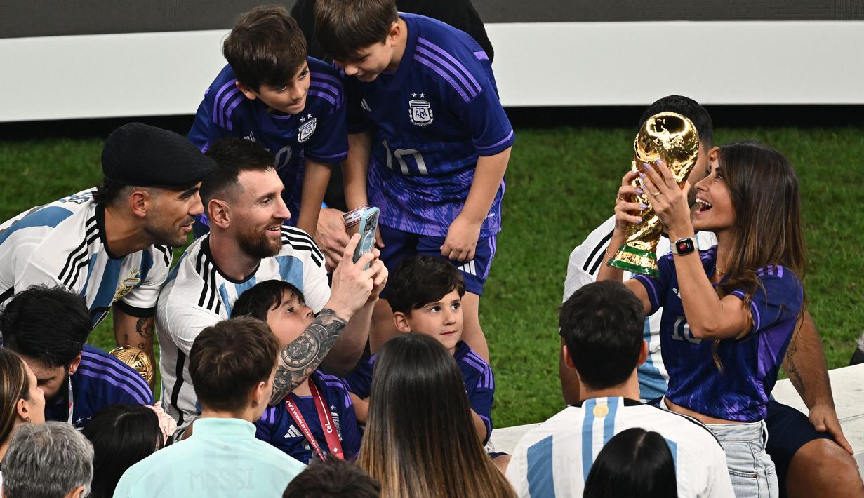 Pemain Argentina, Lionel Messi memotret istrinya, Antonela Ruccuzzo (kanan) yang sedang memegang trofi Piala Dunia 2022 setelah timnya berhasil mengalahkan Prancis pada laga final yang berlangsung di Lusail Stadium, Qatar, Minggu (18/12/2022). Albiceleste menang 4-2 atas Prancis di babak penalti. (AFP/Jewel Samad)