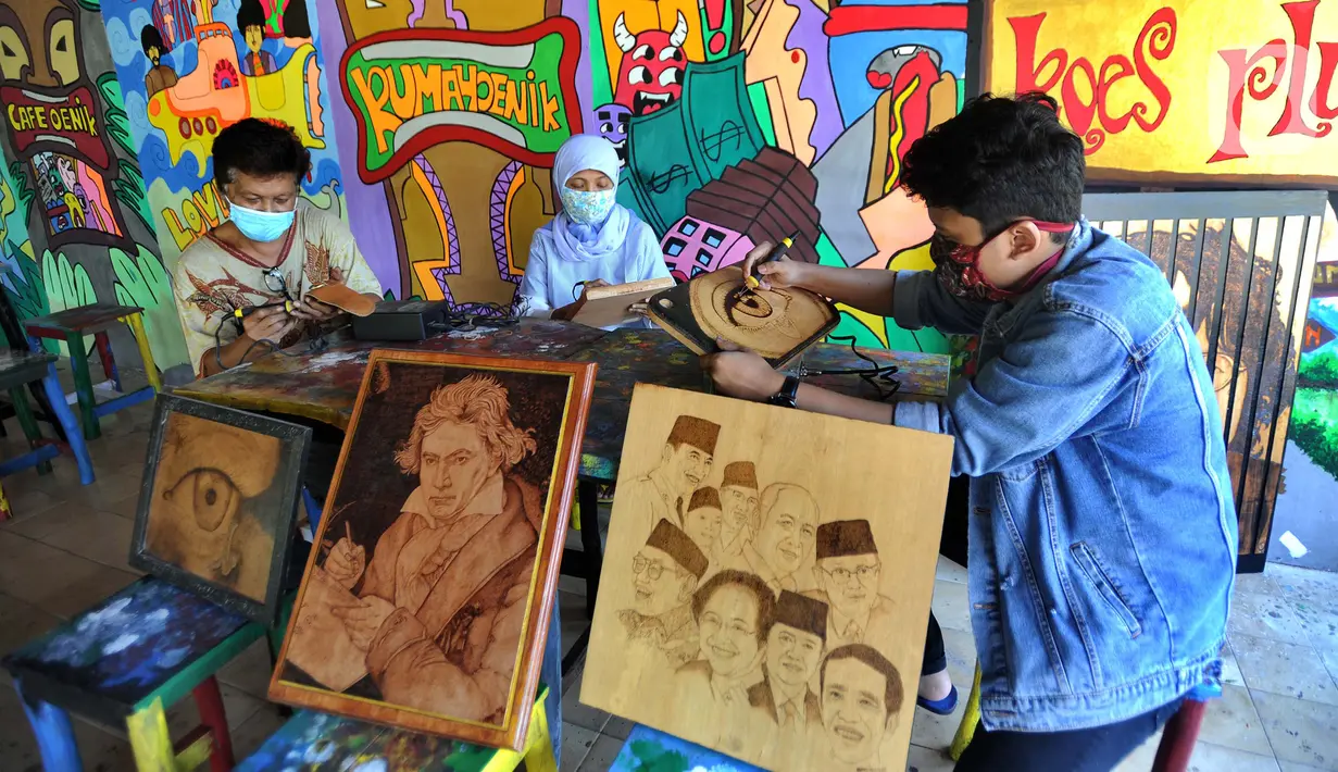 Arfan (55) seniman pelukis bakar atau pyrography bersama anak dan istri menyelesaikan karya seni lukis bakar di atas media kayu dan kulit  di galeri Rumah Oenik, Kampung Ragamukti, Tajur Halang, Bogor, Senin (28/9/2020). (Merdeka.com/Arie Basuki)