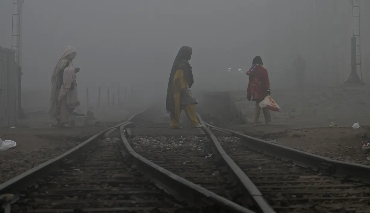 Perempuan melintasi rel kereta api di tengah cuaca berkabut di Lahore (21/12/2022). Kabut tebal kembali menyelimuti berbagai kota di Punjab, termasuk Lahore pada malam hari antara Selasa dan Rabu, melumpuhkan kehidupan sehari-hari dan mengganggu lalu lintas jalan raya dan udara.(AFP/Arif Ali)