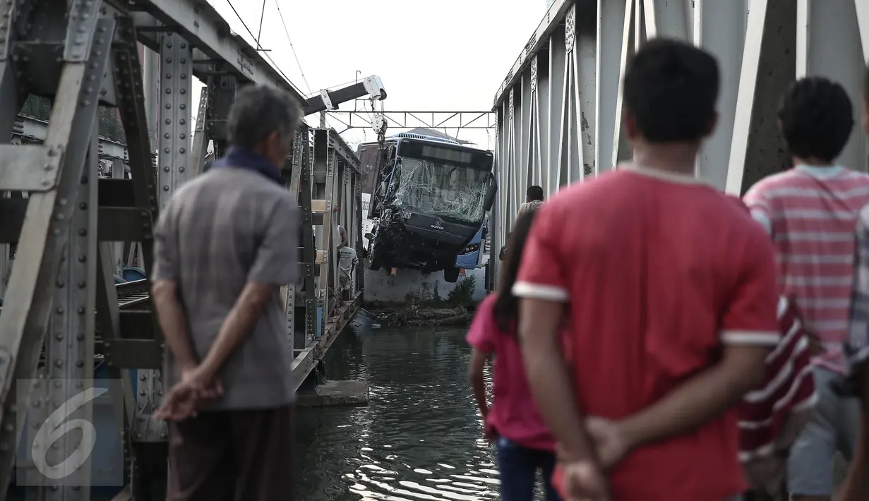 Warga mengamati evakuasi bus TransJakarta yang terperosok ke sungai usai ditabrak kereta api Senja Utama Solo di perlintasan kereta Mangga Dua, Jakarta, Kamis (19/5). Sopir mobil Avanza dan TransJakarta mengalami luka-luka. (Liputan6.com/Faizal Fanani)