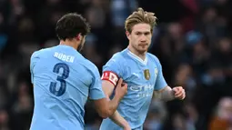 Pemain Manchester City, Ruben Dias (kiri), memberikan ban kapten kepada rekannya yakni Kevin De Bruyne saat memasuki lapangan pada menit ke-57 dalam pertandingan putaran ketiga Piala FA melawan Huddersfield Town yang berlangsung di Etihad Stadium, Manchester, Minggu (7/1/2024). (AFP/Paul Ellis)