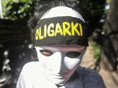 Seorang anak muda yang mengenakan topeng dan ikat kepala bertuliskan "Oligarki" menggelar aksi damai di luar Kantor Komnas HAM, Jakarta, Kamis (14/7/2022). Mereka meminta hak asasi akibat krisis iklim dengan mengadukan kepada Komnas HAM terkait pembiaran krisis Iklim karena sudah sangat berpengaruh pada kehidupan, ekonomi, dan kesehatan perorangan maupun kelompok akibat kenaikan suhu bumi serta cuaca ekstrem. (Liputan6.com/Faizal Fanani)
