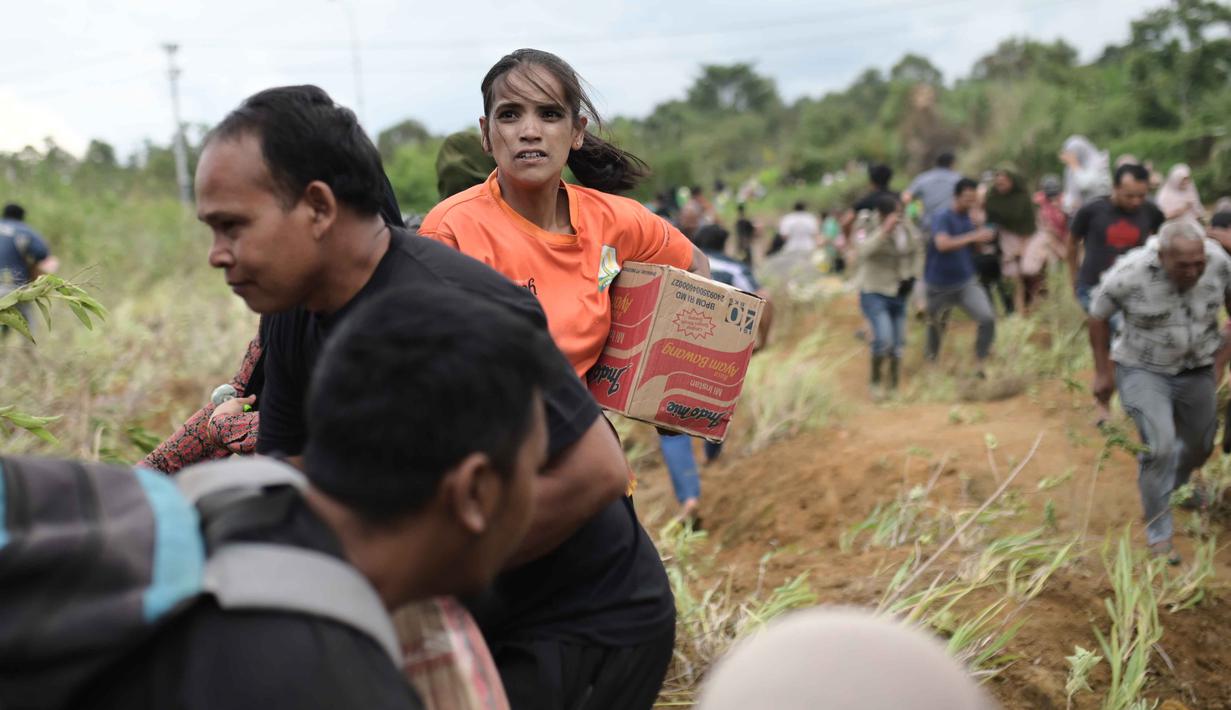 Pemerintah memastikan distribusi bantuan menjangkau seluruh wilayah, termasuk wilayah yang masih terisolir. Tampak dalam foto, para penyintas banjir membawa barang-barang bantuan yang didistribusikan oleh helikopter TNI AU di Aceh Tengah, Sabtu 6 Desember 2025. (AP Photo/Reza Saifullah)